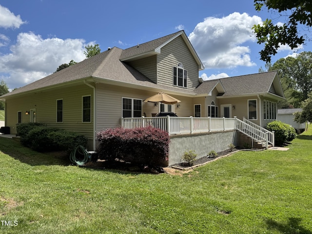 back of property featuring a lawn, roof with shingles, and a deck
