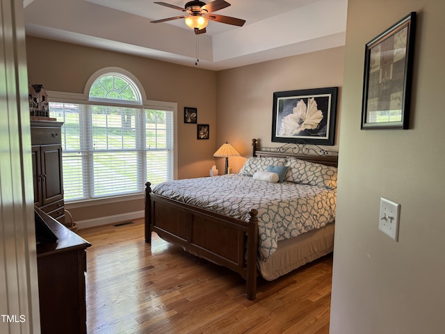 bedroom with wood finished floors, baseboards, ceiling fan, and a raised ceiling