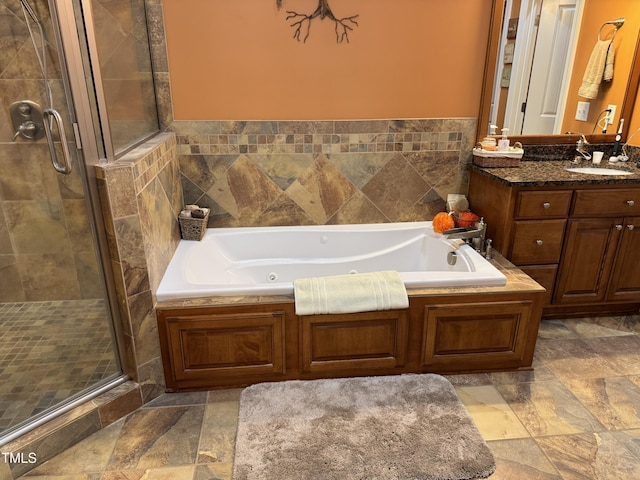 full bathroom with a stall shower, a jetted tub, stone finish floors, and vanity