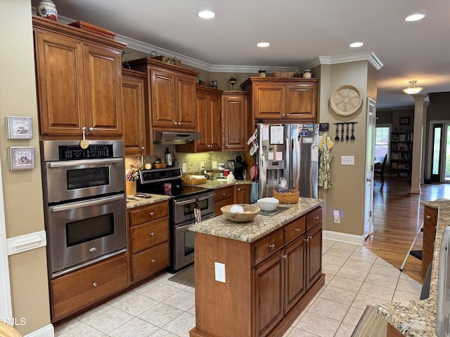 kitchen with appliances with stainless steel finishes, light tile patterned floors, under cabinet range hood, crown molding, and backsplash
