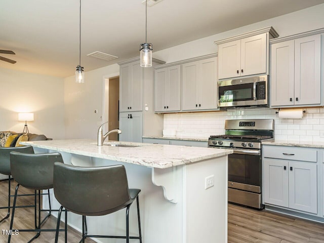 kitchen with stainless steel appliances, a sink, decorative light fixtures, tasteful backsplash, and light stone counters