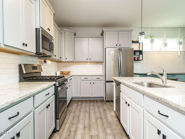 kitchen with stainless steel appliances, a sink, light wood finished floors, decorative backsplash, and light stone counters