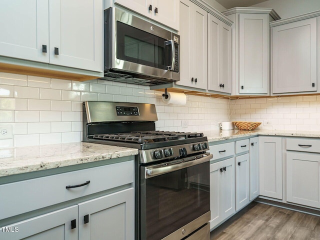 kitchen with stainless steel appliances, tasteful backsplash, wood finished floors, and light stone countertops
