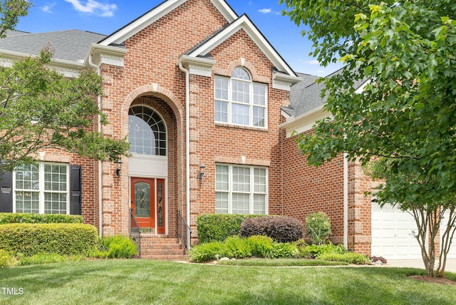 view of front of property with brick siding, an attached garage, a front lawn, and a shingled roof