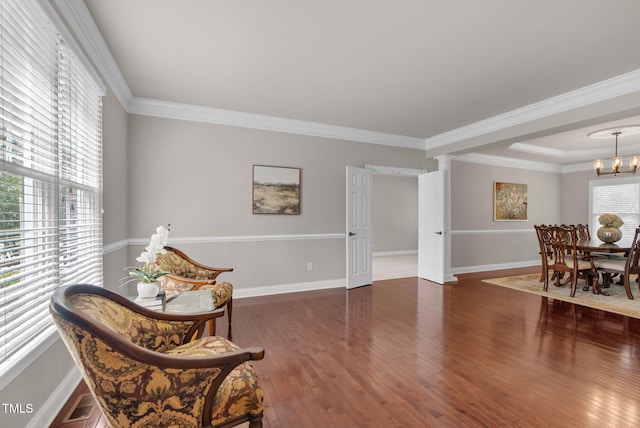 living area with hardwood / wood-style flooring, a chandelier, baseboards, and ornamental molding