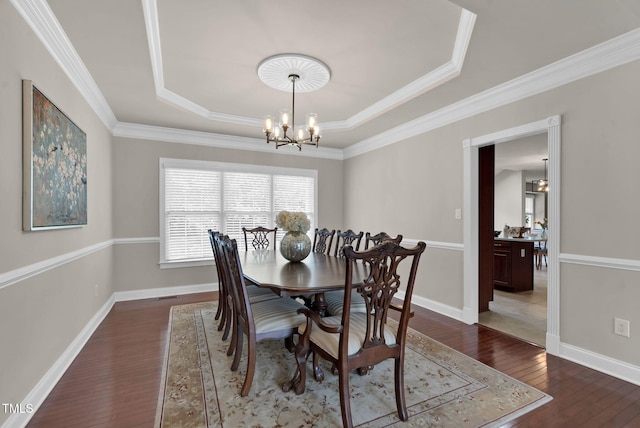 dining space featuring a tray ceiling, a chandelier, wood finished floors, crown molding, and baseboards
