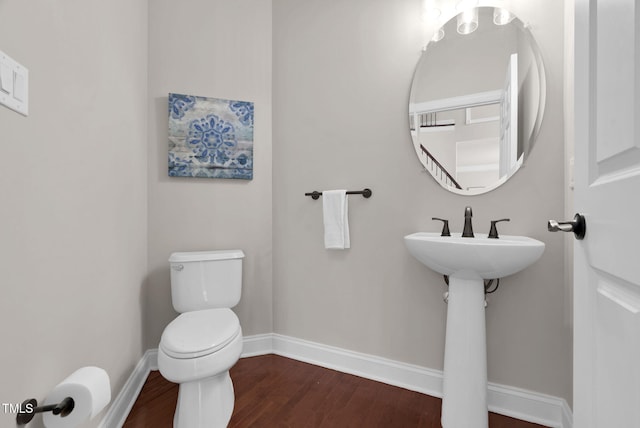 half bathroom with baseboards, wood finished floors, and toilet