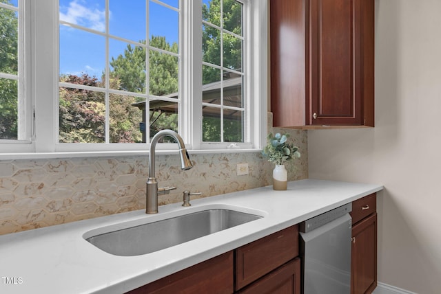 kitchen with stainless steel dishwasher, a sink, decorative backsplash, light countertops, and plenty of natural light