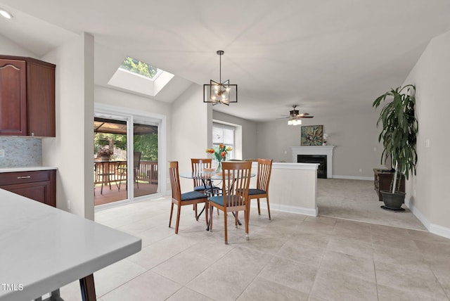dining space featuring vaulted ceiling, a skylight, a fireplace, a chandelier, and ceiling fan