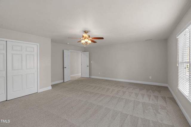unfurnished bedroom featuring light colored carpet, multiple windows, a closet, and ceiling fan