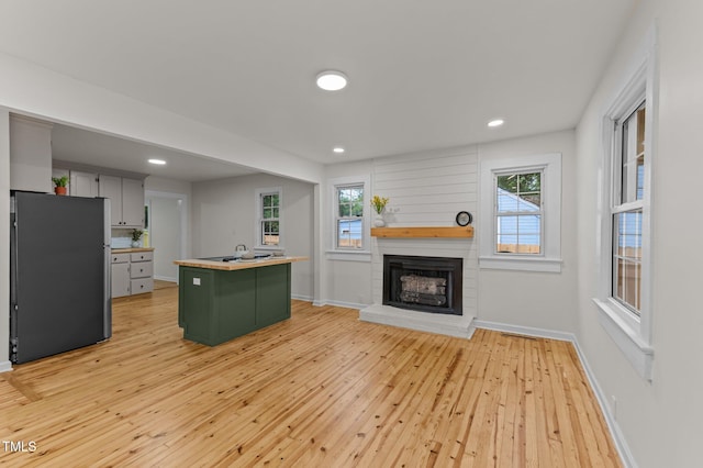 306 Coleman St, Oxford, NC 27565 - kitchen with freestanding refrigerator, a center island with sink, light wood-style floors, green cabinets, and a brick fireplace