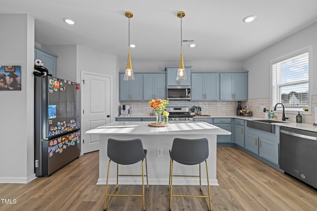 kitchen featuring appliances with stainless steel finishes, a sink, blue cabinets, light countertops, and recessed lighting