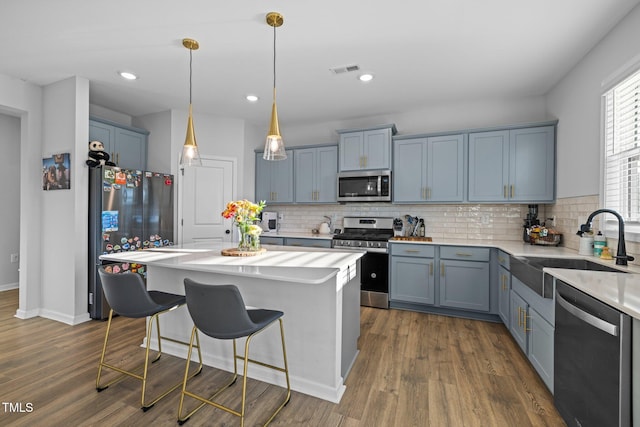 kitchen with stainless steel appliances, a sink, light countertops, a breakfast bar area, and dark wood-type flooring