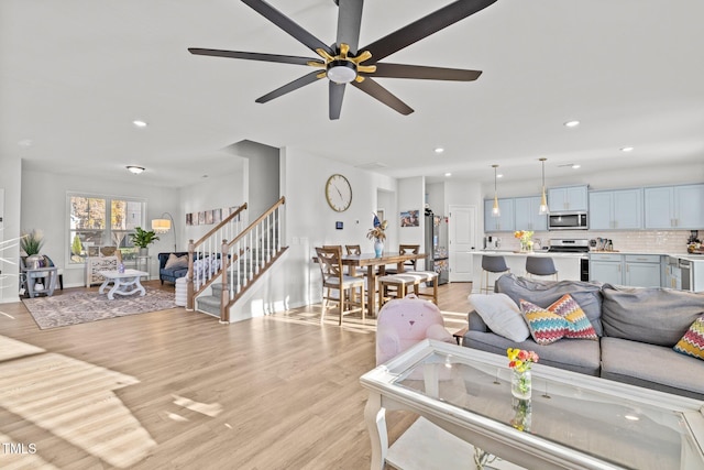 living room with light wood-type flooring, a ceiling fan, recessed lighting, and stairs