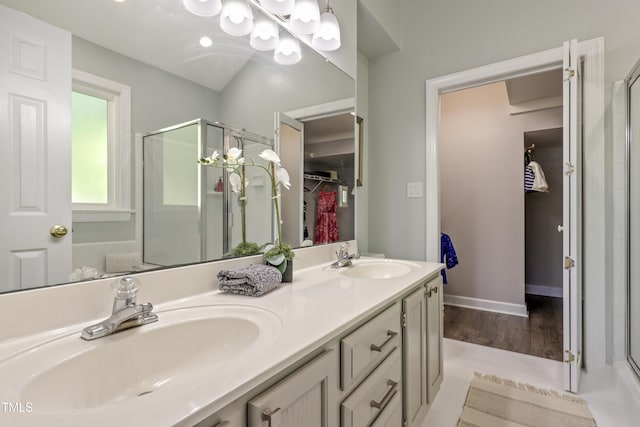 full bathroom with a stall shower, a spacious closet, double vanity, wood finished floors, and baseboards