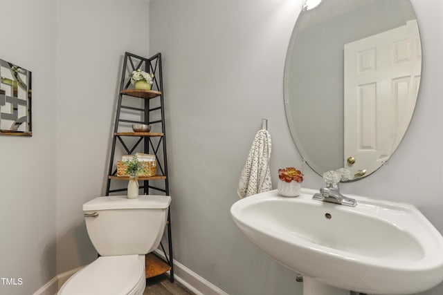half bath featuring a sink, toilet, wood finished floors, and baseboards