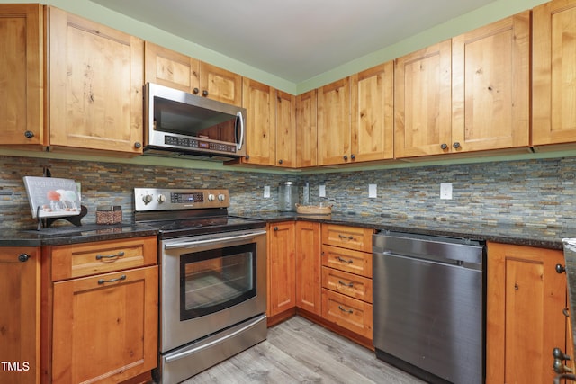 kitchen with appliances with stainless steel finishes, light wood-type flooring, decorative backsplash, and dark stone counters