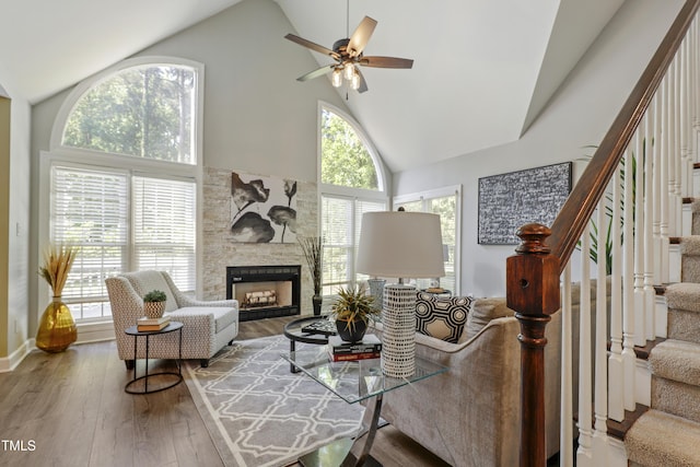 living room with high vaulted ceiling, stairs, a fireplace, hardwood / wood-style floors, and ceiling fan