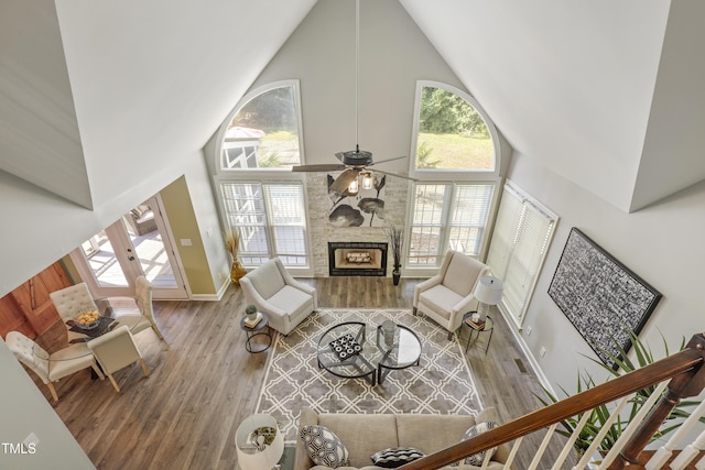 living area with high vaulted ceiling, wood finished floors, a fireplace, a ceiling fan, and baseboards