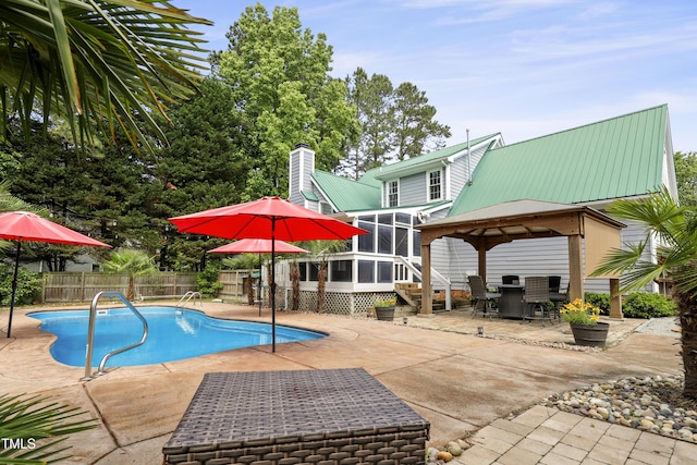 view of swimming pool featuring a sunroom, a patio, a gazebo, fence, and outdoor dining area