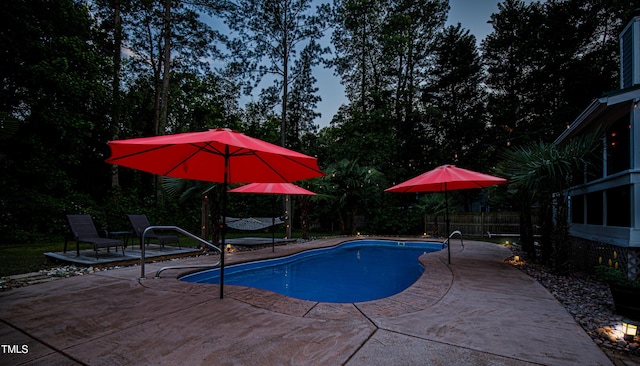 swimming pool featuring a patio, fence, and view of wooded area
