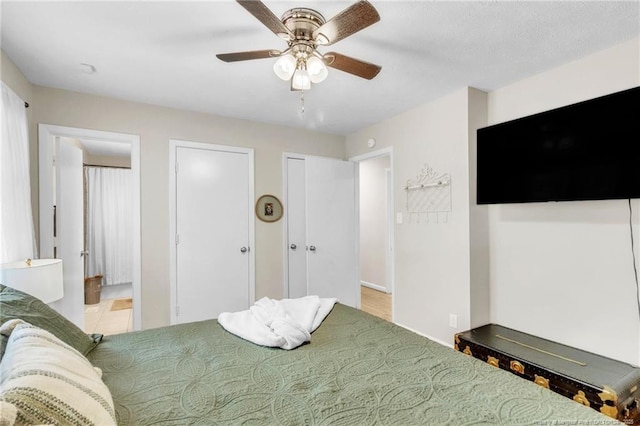 bedroom with two closets, ensuite bathroom, ceiling fan, and baseboards