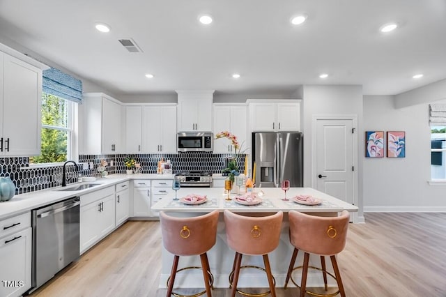 kitchen with appliances with stainless steel finishes, a sink, tasteful backsplash, a kitchen island, and light countertops