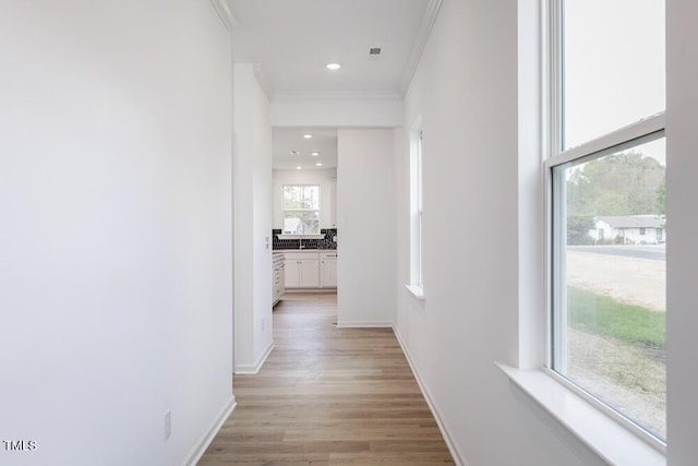 hallway featuring crown molding, baseboards, light wood-style flooring, and recessed lighting