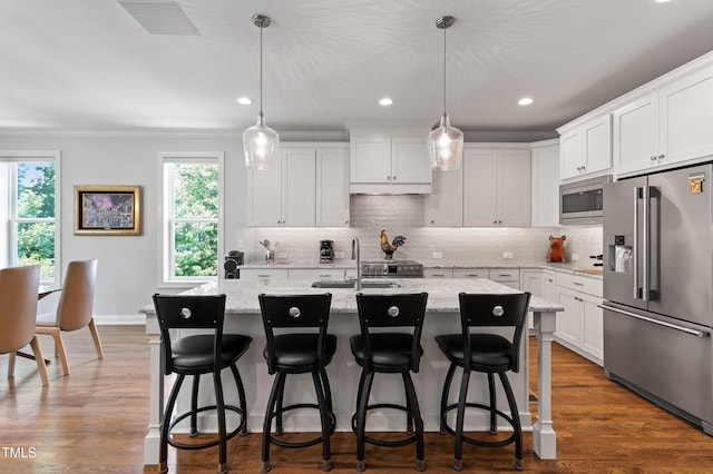 kitchen featuring stainless steel appliances, a sink, ornamental molding, backsplash, and a kitchen island with sink