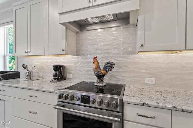 kitchen featuring stainless steel electric range oven, under cabinet range hood, backsplash, and white cabinets