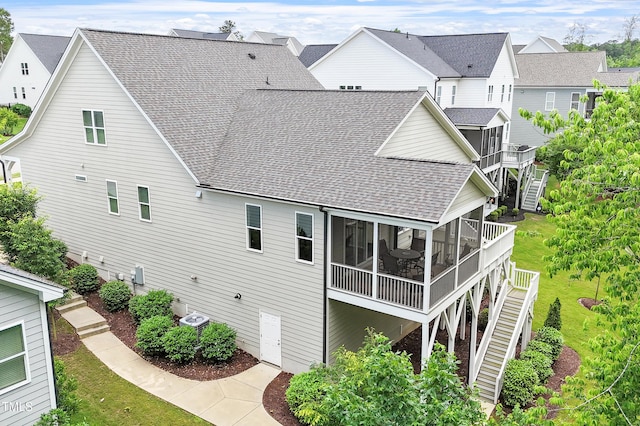 rear view of house with a sunroom, roof with shingles, stairway, and a residential view