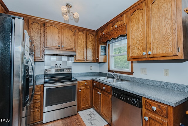 kitchen featuring appliances with stainless steel finishes, a sink, under cabinet range hood, and brown cabinets