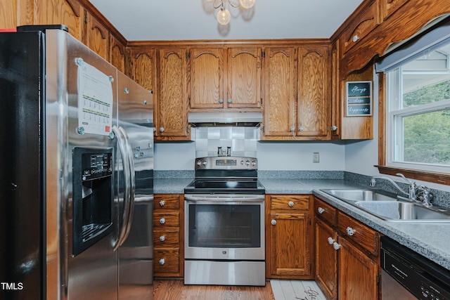 kitchen featuring appliances with stainless steel finishes, a sink, under cabinet range hood, light wood-type flooring, and brown cabinetry