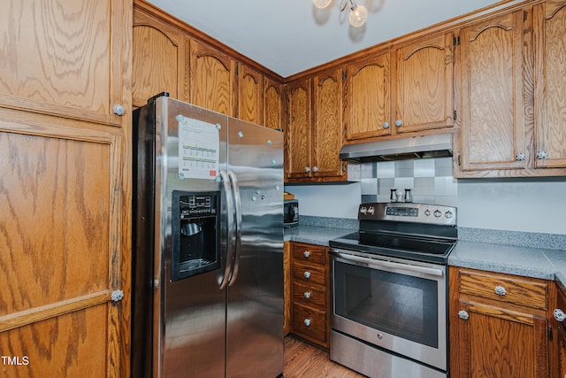 kitchen with appliances with stainless steel finishes, under cabinet range hood, brown cabinetry, and light wood finished floors