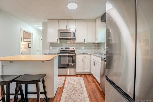 kitchen with appliances with stainless steel finishes, white cabinetry, light wood finished floors, decorative backsplash, and a kitchen bar