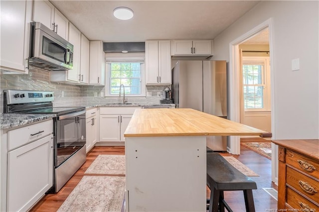 kitchen with appliances with stainless steel finishes, a sink, a kitchen breakfast bar, white cabinetry, and decorative backsplash