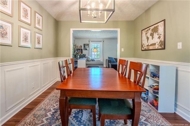 dining space featuring dark wood-type flooring, a chandelier, and a wainscoted wall