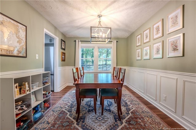dining room with a chandelier, dark wood-type flooring, a textured ceiling, a decorative wall, and wainscoting