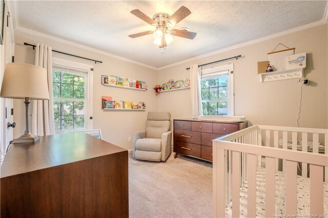 bedroom featuring multiple windows, crown molding, light colored carpet, a crib, and a textured ceiling