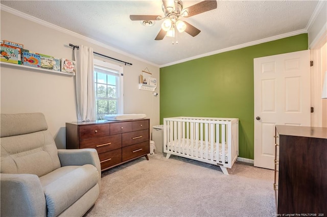 bedroom with crown molding, a crib, light carpet, ceiling fan, and baseboards