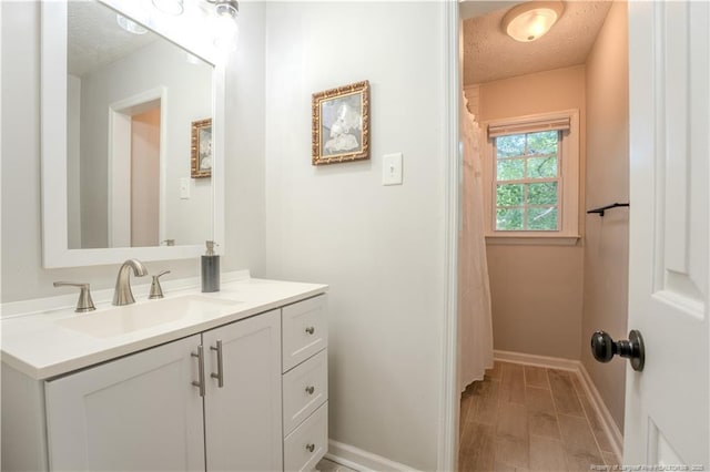 full bathroom featuring a textured ceiling, vanity, and baseboards
