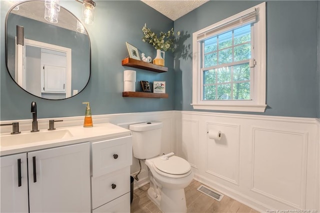 half bath featuring a wainscoted wall, vanity, toilet, wood finished floors, and a decorative wall