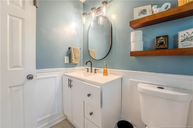 half bathroom featuring a wainscoted wall, vanity, a decorative wall, and toilet