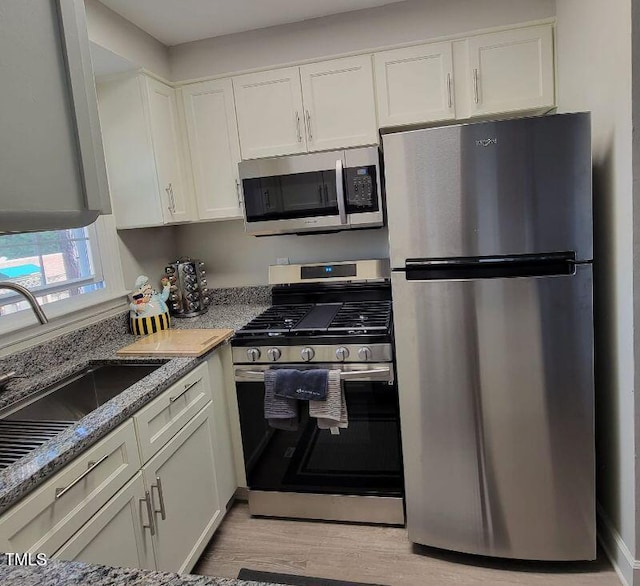 kitchen with appliances with stainless steel finishes, a sink, white cabinetry, and light stone countertops