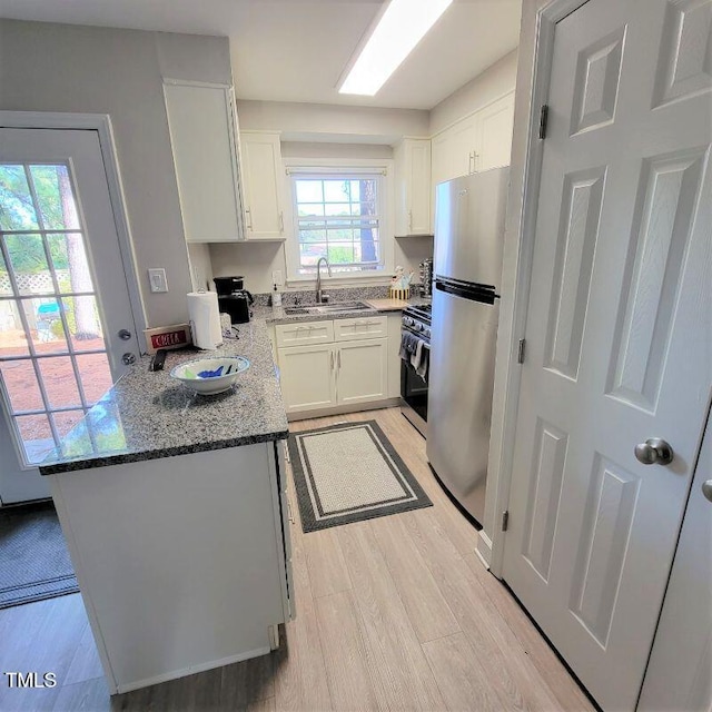 kitchen featuring stainless steel appliances, a sink, light wood-style floors, dark stone counters, and white cabinetry