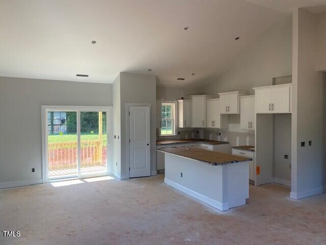 kitchen featuring a center island, white cabinets, baseboards, high vaulted ceiling, and light colored carpet