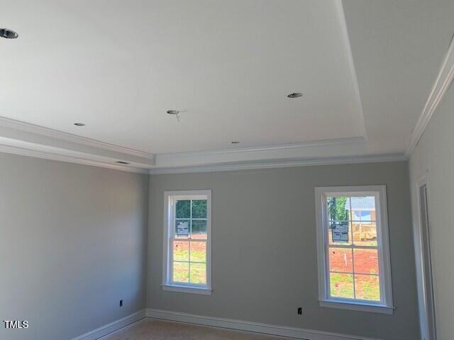 empty room featuring ornamental molding, a tray ceiling, and baseboards