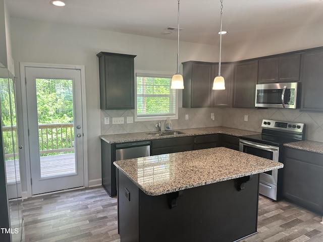kitchen featuring appliances with stainless steel finishes, a sink, light stone counters, light wood finished floors, and a kitchen island