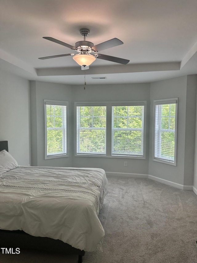 carpeted bedroom featuring baseboards, ceiling fan, and a raised ceiling