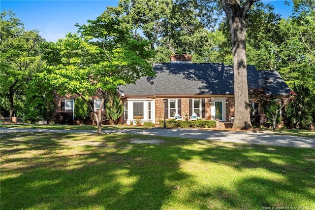 view of front of property with a front lawn, a chimney, brick siding, and a shingled roof